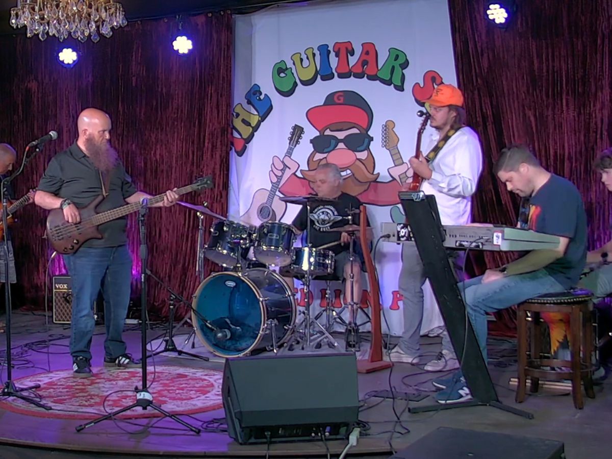 Band Lab students performing together on stage beneath The Guitar Spot banner