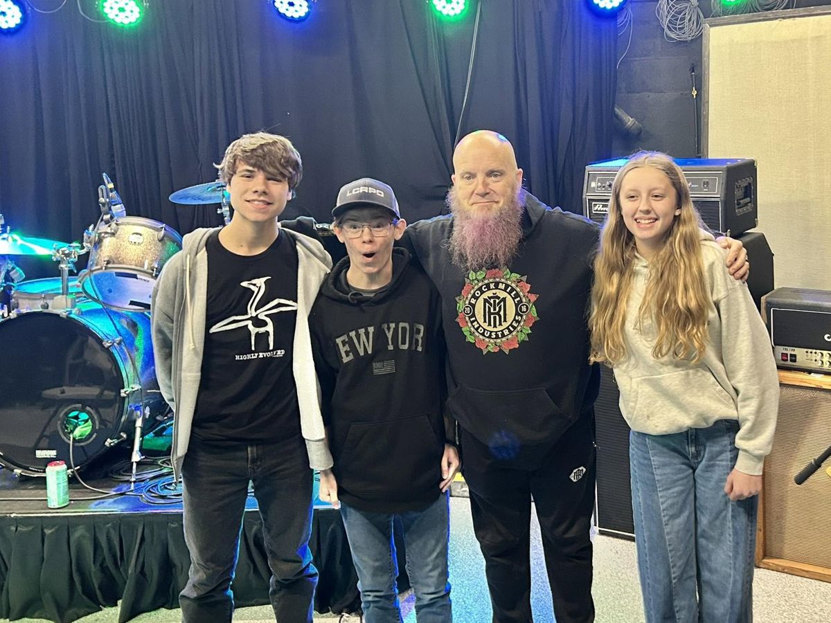 Instructor Rod Goelz with three teenage Band Lab students in front of the stage